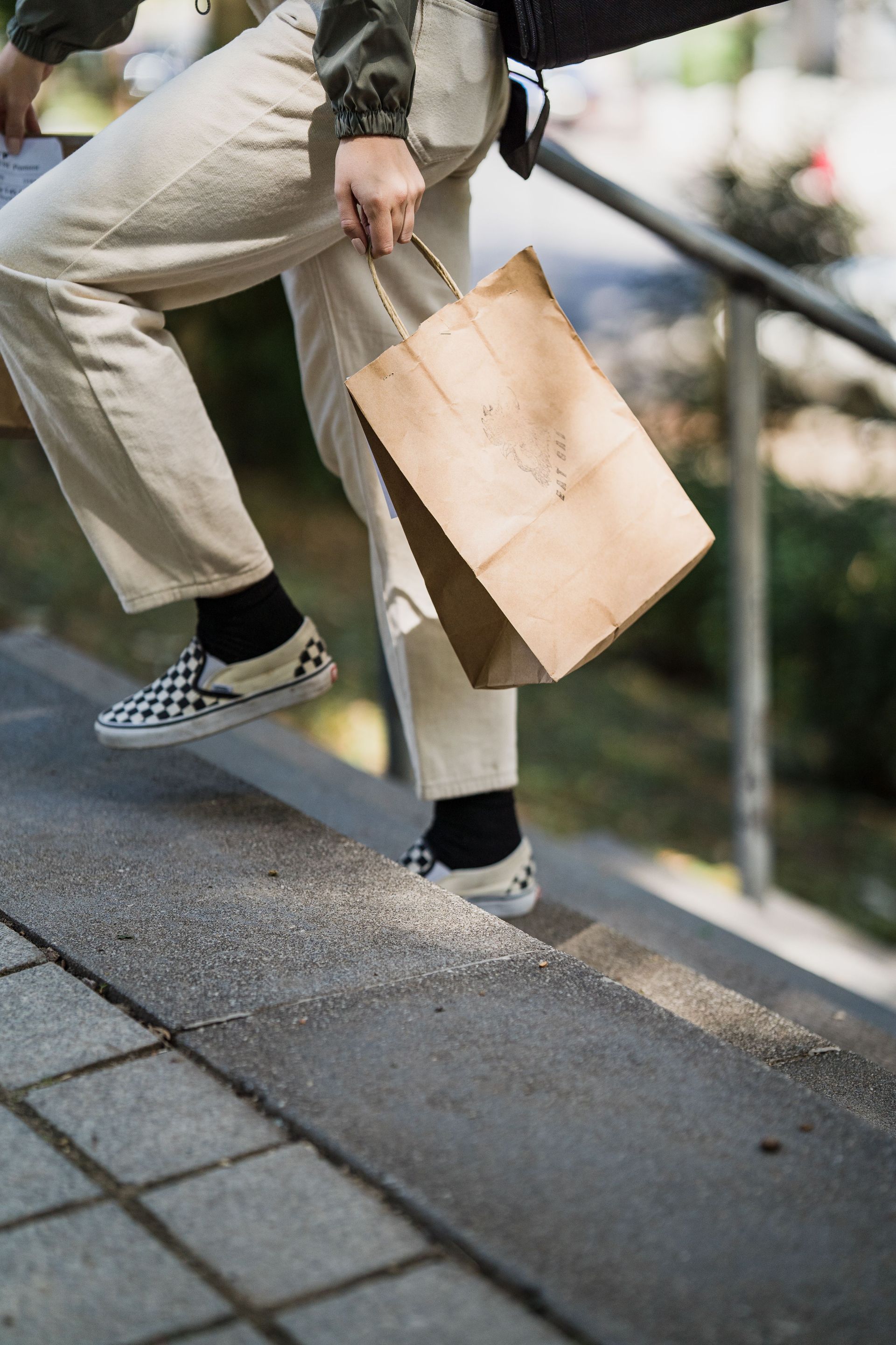 Side view of a woman carrying a paper bag while climbing stairs outdoors, showcasing casual lifestyle.